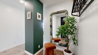 This well-appointed 2-bedroom, 1-bathroom residence combines modern urban design with carefully curated interiors across a single, efficiently laid-out floor. The entryway sets the tone immediately, featuring a bold forest-green accent wall, framed artwork, a statement floor mirror with an ornate frame, and polished concrete flooring that flows throughout much of the home.

The open-concept kitchen and living area forms the heart of the space. The kitchen is outfitted with white cabinetry, dark granite countertops, a black mosaic tile backsplash, stainless steel appliances, and open shelving. A peninsula with bar seating provides additional prep and dining space. Large floor-to-ceiling windows flood the area with natural light and frame impressive city skyline views. The living room echoes this brightness, offering generous ceiling height and a relaxed, modern atmosphere.

The primary bedroom is a spacious retreat, wrapped in expansive windows that showcase panoramic urban views. A glass partition adds an architectural touch while maintaining an open feel. The second bedroom features a vivid teal accent wall and its own window with natural light. The bathroom includes a full tub-shower combination with dark mosaic tile surround and concrete flooring, consistent with the home's cohesive modern aesthetic.