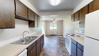 Located at 8719 N Hill n Dale St in Spokane, WA, this two-floor residence offers a practical and well-organized layout across both levels. The kitchen is equipped with dark wood cabinetry, light countertops, a double-basin sink, and white appliances including an electric range and refrigerator. Stone-look tile flooring runs through the kitchen and extends into the adjacent dining and living area, which features a ceiling fan and a wall-mounted HVAC unit beneath a natural-light-providing window. The living spaces are finished with neutral-toned carpet, textured ceilings, and baseboard heating throughout. Bedrooms are carpeted and feature ceiling fans, windows with outdoor views of surrounding greenery, and built-in closets for ample storage. The bathrooms include a full tiled tub-and-shower combination as well as a separate water closet with a window and baseboard heater, both finished with the same durable tile flooring seen in the kitchen. A staircase connects the two floors, as visible in the schematic overview. The overall interior presents a clean, functional aesthetic with consistent finishes, neutral color tones, and practical amenities suited for comfortable everyday living.