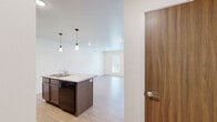 Located at 5102 Shelby Ave in Rapid City, South Dakota, this one-bedroom, one-bathroom residence offers a well-designed single-floor layout with a clean, modern aesthetic. The open-concept kitchen and living area serves as the heart of the home, anchored by a central island with a granite-style countertop, an undermount sink, and pendant lighting above. Rich dark-toned cabinetry lines the kitchen walls, complemented by black appliances including a refrigerator, range, and built-in microwave. Light hardwood-style flooring extends throughout the main living spaces, enhancing the bright, airy feel created by white walls and recessed lighting. The living area features a door that opens to a balcony, bringing in natural light. The bedroom offers plush carpeting, a window for natural light, and ample wall space for furnishings. The bathroom includes a granite-topped vanity with dark cabinetry, a full soaking tub, and hardwood-style flooring, with a window that adds ventilation and brightness. A laundry area is also visible within the bathroom corridor, adding everyday convenience to this thoughtfully arranged residence.