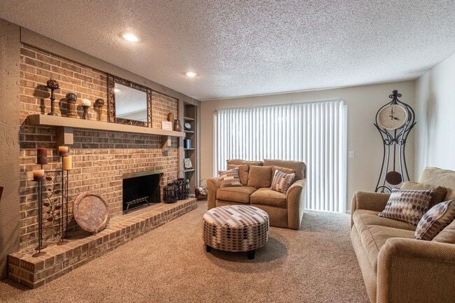 A cozy living room featuring a three-seater sofa, love seat, a fireplace, a floor clock, and a round coffee table, all bathed in warm lighting for the perfect, inviting space. - Wilshire Apartments