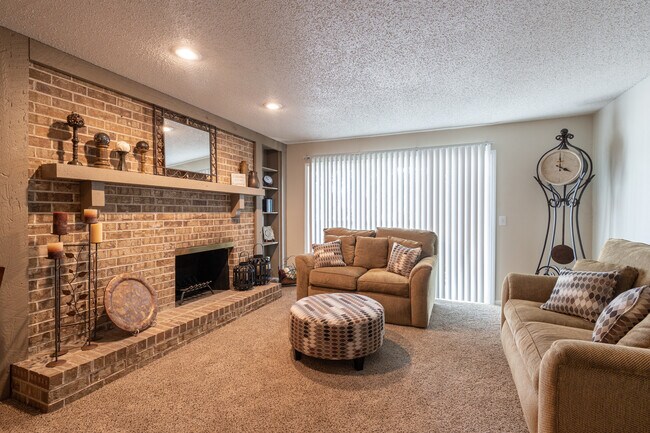 Una acogedora sala de estar con un sofá de tres plazas, un sofá de dos plazas, una chimenea, un reloj de pie y una mesa de café redonda, todo bañado por una iluminación cálida para crear un espacio perfecto y acogedor. - Wilshire Apartments