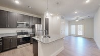 Located in Mesquite, Texas, this single-story 2-bedroom, 2-bathroom home offers a clean, modern aesthetic with light wood-look flooring and neutral tones throughout. The open-concept kitchen is a standout feature, equipped with dark espresso shaker-style cabinetry, granite countertops, stainless steel appliances including a range, microwave, and refrigerator, and a central island with an undermount sink and pendant lighting above — ideal for both cooking and entertaining. Ample upper and lower cabinetry provides generous storage space. The bedrooms are bright and comfortable, with the primary bedroom featuring a ceiling fan and a large window that brings in natural light and outdoor views. Both bathrooms are thoughtfully designed with dark wood vanities, granite countertops, and wood-look flooring. One bathroom includes a soaking tub and shower combination, while the other features accessible grab bars. Each bedroom connects to its own walk-in closet, fitted with multi-level shelving and hanging rods for organized storage. Throughout the home, crisp white panel doors, clean baseboards, and a consistent light color palette create a cohesive and inviting atmosphere.