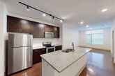 Located at Century Square in College Station, TX, this one-bedroom, one-bathroom unit offers a thoughtfully designed layout across a single floor. The open-concept kitchen serves as a focal point, showcasing rich dark espresso cabinetry, gleaming granite countertops, a double undermount sink, and a full suite of stainless steel appliances including a refrigerator, range, and built-in microwave. Track and recessed lighting illuminate the space, while warm hardwood-style flooring adds depth and continuity throughout the main living areas. The living area is bright and open, benefiting from natural light through large windows fitted with horizontal blinds. The bedroom is carpeted for comfort, features a ceiling fan, and receives ample natural light through a generously sized window. A dedicated closet provides convenient storage. The full bathroom is well-appointed with large-format tile flooring, a granite-topped dark wood vanity, a framed mirror, and a glass-enclosed walk-in shower, with a window that brings in additional natural light. Clean white walls and modern finishes throughout create a cohesive, contemporary ambiance well-suited for everyday living.