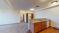 Located at 5317 South Palouse in Spokane, Washington, unit F145 is a single-floor residence thoughtfully designed for comfortable, everyday living. The open-concept layout connects the kitchen and living area seamlessly, creating a spacious and functional common space. The kitchen features warm honey-toned wood cabinetry, a double-basin stainless steel sink, a tile backsplash, a full suite of white appliances including a range, dishwasher, and refrigerator, and durable hardwood-style flooring. A peninsula counter provides a natural division between the kitchen and the carpeted living area, which benefits from a private entry door and a transom window that brings in natural light. The living space flows into a hallway that leads to the bedroom and additional rooms. The bedroom is comfortably sized with plush carpeting, a large window overlooking the exterior, and a baseboard heating unit. The bathroom includes a full tub-shower combination with clean white surround, a wood-cabinet vanity, and tile flooring. A standout feature of this unit is the in-unit laundry area, adding significant everyday convenience. The accessible electrical panel and consistent neutral tones throughout contribute to a clean, move-in-ready atmosphere.