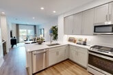 This thoughtfully designed one-bedroom, one-bathroom residence offers a cohesive open-concept layout finished with warm light wood flooring and a neutral color palette throughout. The kitchen serves as a central hub of the living space, featuring sleek gray shaker-style cabinetry, white quartz countertops, stainless steel appliances including a dishwasher and range, and a peninsula with an undermount sink — ideal for both cooking and casual dining. The kitchen flows seamlessly into the living and dining areas, which are bathed in natural light from large windows and a glass door leading to a private balcony with outdoor views.

The bedroom is a comfortable retreat, highlighted by a large window with exterior views, soft gray walls, and direct access to a well-organized walk-in closet equipped with built-in shelving and multiple hanging rails. The full bathroom features large-format gray tile flooring, a wood-toned vanity with a white quartz countertop, and a full tub-shower combination with tile surround. Recessed lighting throughout the home adds a clean, modern touch, while the consistent use of quality materials creates a polished and functional living environment from room to room.