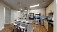 Located at 800 Timber Valley Way in Oakwood, Georgia, this single-floor residence showcases a contemporary design with a cohesive neutral color palette and warm wood-look flooring throughout. The open-concept layout connects the kitchen, dining, and living areas seamlessly, creating an airy, functional flow.

The kitchen is a standout feature, equipped with stainless steel appliances including a French door refrigerator, range, microwave, and dishwasher. Light wood cabinetry pairs with subway tile backsplash and a central island topped with a light quartz countertop, offering bar seating for two. Pendant lighting with brushed nickel fixtures adds an industrial-modern touch overhead.

The living room provides a comfortable retreat with a ceiling fan, large french doors that invite natural light, and ample space for relaxed seating arrangements. The entryway offers a welcoming transition into the open living spaces.

The bedroom features multiple windows dressed with sheer curtains, allowing generous natural light, alongside wood-tone furnishings that complement the warm flooring. The bathroom includes a tub-shower combo with classic white subway tile surround, dark countertop vanity, and wood-look flooring, maintaining the consistent modern aesthetic found throughout the residence.