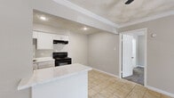 This well-organized one-bedroom, one-bathroom unit makes smart use of its single-floor layout, offering a cohesive and functional living space finished in soft, neutral tones throughout. The kitchen is a standout feature, equipped with white cabinetry, a black electric range with overhead ventilation, and a peninsula topped with a marble-look surface — ideal for meal prep or casual dining. Crown molding and recessed lighting add a refined touch to the kitchen ceiling. Light beige tile flooring runs through the kitchen, living area, bathroom, and closet, lending a clean, consistent look. The living room offers an open, adaptable space that flows naturally from the kitchen. The bedroom is a comfortable retreat, carpeted for warmth and featuring a ceiling fan with light fixture, a window with blinds that brings in natural light, and soft textured ceiling detail. A dedicated walk-in closet off the bedroom provides dual hanging rods and shelving on both sides, maximizing storage. The bathroom includes a full soaking tub with a tiled shower surround, a toilet, and a marble-topped vanity, all finished in crisp white. The overall ambiance is clean, understated, and move-in ready.