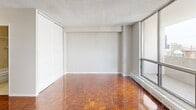 Located at 545 Sherbourne Street in Toronto's St. James Town neighbourhood, this efficiently designed unit offers a thoughtful layout comprising a living room, kitchen, bathroom, and a private balcony. The living room is a standout feature, showcasing rich, polished parquet wood flooring in a classic herringbone-style pattern that adds warmth and character to the space. Floor-to-ceiling windows flood the room with natural light and provide open city views, while a baseboard heating unit runs along the exterior wall. The textured ceiling adds a traditional touch consistent with the building's established character. The kitchen is compact yet functional, outfitted with white cabinetry, a marble-look countertop, a subway tile backsplash, and a stainless steel electric range, offering everything needed for everyday cooking. The bathroom is clean and practical, featuring light tile flooring, a white vanity with a marble-look countertop, a large mirror with overhead lighting, and a tiled shower-tub combination. The balcony extends the living space outdoors, providing a private spot to enjoy the surrounding urban skyline. Overall, the unit presents a bright, functional living environment well-suited to those seeking a manageable footprint in a central Toronto location.