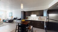 Located at 350 W Lucy Ave in Salt Lake City, Utah, this single-floor residence offers a well-designed layout with modern finishes throughout. The kitchen is a standout feature, showcasing rich dark espresso cabinetry that extends to the ceiling, contrasting light countertops, black appliances including a full-size refrigerator and range, an under-cabinet lighting system, and a deep single-basin sink. A movable kitchen island with bar seating provides additional prep space and casual dining options. Light wood-style flooring runs through the main living areas, adding warmth and continuity to the space. The living room is bright and welcoming, benefiting from multiple windows that allow generous natural light to fill the room. A wall-mounted television, open layout, and a dedicated dining nook make the space both functional and versatile. The bedroom offers carpeted flooring for comfort, a window with exterior views, and ample room for furnishings. The full bathroom is finished with clean white tile in the tub-shower surround, light wood-style flooring, dark vanity cabinetry, and white countertops, creating a crisp and tidy aesthetic. Overall, the unit presents a cohesive contemporary design with practical functionality throughout.