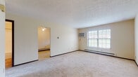 Located at 367 Waterside Ave in Canal Fulton, Ohio, this single-floor residence offers a functional and straightforward layout designed for comfortable everyday living. The main living area is generously proportioned, featuring wall-to-wall carpeting in neutral tones, a textured ceiling, and a large multi-pane window that allows ample natural light to fill the room. A wall-mounted air conditioning unit and baseboard heating ensure year-round comfort. Dark wood trim accents throughout the space provide a clean visual contrast against the light-colored walls. Adjacent to the living area, a secondary room — accessible through a ceiling fan-equipped passageway — offers additional flexible living space. The bedrooms continue the carpeted, light-toned aesthetic, each featuring dark wood doors and trim with views into the connected living spaces. One bedroom includes a vaulted ceiling detail near a stairway, along with a spacious walk-in closet with built-in shelving, adding notable storage capacity. The full bathroom is finished with tile flooring, a tiled tub-and-shower combination, a single-sink vanity with cabinetry, and a medicine cabinet, maintaining a clean and practical design throughout. Overall, the residence presents a well-maintained, move-in-ready interior in a quiet Canal Fulton neighborhood setting.