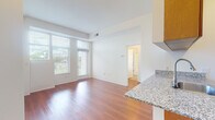 This single-floor residence offers a well-designed layout that balances open communal spaces with functional private areas. The living area is a standout feature, highlighted by large floor-to-ceiling windows fitted with horizontal blinds that invite abundant natural light while offering outdoor views of surrounding greenery. A glass door provides direct access to a private balcony, further enhancing the connection to the outdoors. Rich hardwood flooring runs throughout the main living and kitchen areas, contributing warmth and continuity to the space.

The kitchen is thoughtfully designed in a galley configuration, featuring warm-toned wood cabinetry that extends to the ceiling for generous storage. Granite countertops with a speckled pattern are carried throughout, including along a breakfast bar that opens toward the living area. Black appliances, including a refrigerator, electric range, built-in microwave, and dishwasher, complete the functional kitchen setup.

The bedroom is carpeted and generously sized, with a large window that brings in natural light and outdoor views. The bathroom is clean and straightforward, featuring tile flooring, a wood vanity with matching granite countertop, and a full tub-shower combination. White walls throughout the unit create a bright, neutral backdrop.