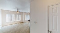 This single-floor residence offers a thoughtfully designed layout with a variety of functional living spaces. The main living area is generously proportioned, featuring plush carpeting, vaulted ceilings, and an abundance of natural light streaming through multiple large windows dressed with vertical blinds. A ceiling fan with a light fixture adds both comfort and character, while track lighting provides additional ambiance. The space opens to a sliding glass door, extending the feel of the room further.

The kitchen is well-appointed with rich, warm-toned wood cabinetry, dark granite-style countertops, and a full suite of white appliances including a refrigerator, electric range, and built-in microwave. Track lighting illuminates the workspace, and hardwood flooring adds warmth throughout. A peninsula with additional counter space enhances both functionality and flow.

The bathroom features a warm wood vanity with dual mirrors, granite-style countertops, and a bright vanity light bar. Hardwood flooring continues here, complementing the cohesive design. Adjacent to the bathroom, a dedicated in-unit laundry room houses a full-size washer and dryer alongside a water heater, with shelving above for added storage.

A spacious walk-in closet provides ample organization with multiple hanging rods and built-in shelving units, alongside a convenient built-in desk with granite-style surface — ideal as a compact workspace.