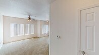 This single-floor residence offers a thoughtfully designed layout with a variety of functional living spaces. The main living area is generously proportioned, featuring plush carpeting, vaulted ceilings, and an abundance of natural light streaming through multiple large windows dressed with vertical blinds. A ceiling fan with a light fixture adds both comfort and character, while track lighting provides additional ambiance. The space opens to a sliding glass door, extending the feel of the room further.

The kitchen is well-appointed with rich, warm-toned wood cabinetry, dark granite-style countertops, and a full suite of white appliances including a refrigerator, electric range, and built-in microwave. Track lighting illuminates the workspace, and hardwood flooring adds warmth throughout. A peninsula with additional counter space enhances both functionality and flow.

The bathroom features a warm wood vanity with dual mirrors, granite-style countertops, and a bright vanity light bar. Hardwood flooring continues here, complementing the cohesive design. Adjacent to the bathroom, a dedicated in-unit laundry room houses a full-size washer and dryer alongside a water heater, with shelving above for added storage.

A spacious walk-in closet provides ample organization with multiple hanging rods and built-in shelving units, alongside a convenient built-in desk with granite-style surface — ideal as a compact workspace.