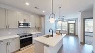 This well-designed one-bedroom, one-bathroom residence at 2500 Pelham Rd in Greenville, SC offers a thoughtfully arranged single-floor layout that maximizes every square foot. The open-concept living and kitchen area serves as the heart of the home, with warm light wood-style flooring and a ceiling fan overhead. The kitchen is a standout feature, showcasing soft gray shaker cabinetry, white quartz countertops, a tile backsplash, and stainless steel appliances including a French door refrigerator, electric range, and built-in microwave. A central island with a matte black faucet and undermount sink provides additional prep space and seating. Pendant globe lights suspended on matte black fixtures add a contemporary touch. The living area receives ample natural light through multiple windows and offers direct access to a private balcony. The bedroom features plush carpet flooring, a ceiling fan, and a large window with outdoor views. Three closets provide generous storage throughout the unit. The bathroom impresses with a double-sink vanity, white quartz countertops, dark-framed mirrors, and light wood-style flooring, conveying a clean, modern aesthetic throughout this Greenville residence.