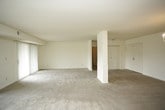This single-floor residence offers a clean, neutral aesthetic with a practical and functional layout. The open living area is expansive, finished with plush wall-to-wall carpeting and anchored by an elegant chandelier that adds a touch of warmth to the space. A central dividing wall partially separates the living and dining areas while maintaining an open flow, and vertical blinds over sliding glass doors allow for abundant natural light and outdoor access. The kitchen is efficiently designed with dark wood cabinetry, dark countertops, tile flooring, and full appliances including an electric range and refrigerator. A tall pantry cabinet provides additional storage. The bedroom is generously sized, also carpeted, and features sliding mirrored closet doors that enhance the sense of space, along with a sliding glass door that connects to an outdoor area. The bathroom is thoughtfully appointed with a double-sink vanity topped with a marble-style countertop, dark wood cabinetry with ample drawer storage, a louvered wall vent, and a separate water closet containing a tiled tub-shower combination. A spacious walk-in closet with a full-length hanging rod and shelf completes the bedroom suite, offering substantial storage capacity throughout.