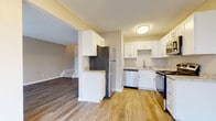 This two-story home offers a thoughtfully designed layout with a blend of practical finishes and comfortable living spaces across both levels. The kitchen serves as a functional centerpiece, featuring white shaker-style cabinetry, granite-look countertops, and a full suite of stainless steel appliances including a refrigerator, dishwasher, gas range, and microwave. Light wood-tone vinyl plank flooring runs through the kitchen and connects seamlessly to the main living areas, which are bright and open with multiple windows allowing natural light to fill the space. The living area provides a generous, open layout with a front entry door and views to an adjacent room, creating an easy flow throughout the main floor. A staircase leads to the upper level, where the bedrooms are finished with plush neutral carpeting and windows that bring in additional natural light. The bathroom features a white vanity with granite-look countertops, brushed nickel fixtures, and a clean, minimalist design. Textured ceilings are present throughout the home, complementing the warm, neutral wall tones that create a cohesive and inviting atmosphere across all rooms.