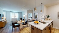 This thoughtfully designed single-floor residence showcases a seamless open-concept layout that connects the kitchen, dining, and living areas into one cohesive, light-filled space. The kitchen is a standout feature, equipped with stainless steel appliances, a gas range, built-in microwave, and a generous island with a quartz countertop and warm wood cabinetry, complemented by sleek pendant lighting overhead. White upper cabinets and light hardwood-style flooring add brightness and continuity throughout the common areas.

The living room offers a comfortable, modern atmosphere with large windows dressed in sheer curtains that invite natural light and frame views of palm trees outside. Multiple bedrooms provide private retreats, each carpeted and fitted with ceiling fans or track lighting, large windows, and ample space. The primary suite includes a walk-in closet and an ensuite bathroom featuring dual sinks, quartz countertops, warm wood vanity cabinetry, and backlit LED mirrors. A second full bathroom mirrors the same refined aesthetic. The overall ambiance is contemporary and welcoming, with a neutral color palette, quality finishes, and a cohesive design language that flows throughout every room.