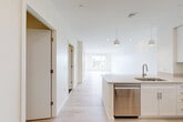 Located at 46 Soldiers Field Place in Boston, MA, this thoughtfully designed one-bedroom, one-bathroom residence offers a clean, modern aesthetic throughout. Light hardwood flooring flows seamlessly across the open floor plan, enhancing the bright and airy atmosphere created by white walls and recessed lighting.

The kitchen is a standout feature, equipped with stainless steel appliances including a range, microwave, dishwasher, and refrigerator, all complemented by crisp white cabinetry, quartz countertops, and pendant lighting above the island. The kitchen opens directly into the dining and living area, making the space ideal for everyday living and entertaining.

The bedroom is generously sized, bathed in natural light from large windows that frame views of surrounding greenery and the Boston cityscape. A versatile den provides additional flexible living space. Two well-appointed closets, including a spacious walk-in with wire shelving, offer ample storage.

The bathroom features a clean, contemporary design with dark tile flooring, a white subway-tiled walk-in shower with a glass door, and a modern floating vanity with a wide mirror. The overall ambiance of this residence is bright, minimalist, and functional, reflecting modern urban living in a well-connected Boston neighborhood.