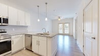Located at 11310 Vandelay Ct in Charlotte, NC, this single-floor residence offers a clean, modern aesthetic throughout. The open-concept layout seamlessly connects the kitchen and living area, creating a bright and airy atmosphere enhanced by light-toned luxury vinyl plank flooring.

The kitchen is well-appointed with crisp white cabinetry, granite countertops, and a full suite of stainless steel appliances including a range, microwave, dishwasher, and refrigerator. A central island with an undermount sink and pendant lighting above adds both functionality and style. The living area extends naturally from the kitchen and is finished with a ceiling fan and French doors that invite natural light and outdoor views.

The bedrooms are carpeted for comfort, each featuring large windows with blinds that allow ample natural light while maintaining privacy. Ceiling fans provide additional comfort in the primary bedroom.

The bathroom is outfitted with white cabinetry, granite countertops, a large vanity mirror, and light wood-look tile flooring. Accessibility-friendly grab bars are thoughtfully installed. Additional interior spaces include a utility area with multiple doors providing organized storage and closet access. Throughout, the residence maintains a neutral, contemporary palette that is both versatile and inviting.