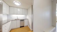 Located on Wellington Street West in Ottawa's vibrant Hintonburg neighbourhood, this 2-bedroom, 1-bathroom unit offers a clean, modern aesthetic throughout its single-floor layout. Light hardwood-style flooring runs continuously across the living areas and bedrooms, creating a cohesive and easy-to-maintain interior.

The kitchen is efficiently designed in a U-shaped configuration, outfitted with sleek, flat-front white cabinetry that extends to the ceiling for generous storage. Under-cabinet lighting illuminates the light-toned countertops, and stainless steel appliances — including a dishwasher and refrigerator — complete the functional space. A subway tile backsplash adds a clean, contemporary touch.

The spacious primary bedroom is a standout feature of the unit, offering generous room for furnishings. It benefits from large windows that allow ample natural light and provide views of the surrounding cityscape. A baseboard heating system runs along the exterior wall. The second bedroom is well-proportioned and includes a built-in sliding door closet, making smart use of the available space.

Two hallways connect the rooms in an organized layout, leading to a full bathroom. The unit's neutral colour palette of soft whites and warm greys throughout lends a bright, airy ambiance, making the overall space feel open and inviting.
