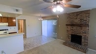 This single-floor home offers a welcoming and functional layout that combines comfort with classic design elements. The main living area is anchored by a full brick fireplace, serving as a striking focal point that adds warmth and character to the room. A ceiling fan with an integrated light fixture is centered overhead, providing both airflow and ambient lighting. Flooring transitions naturally from tile in the entryway and adjoining areas to carpet in the living space, creating distinct yet connected zones. A large sliding glass door fitted with vertical blinds allows abundant natural light to pour into the room while offering access to the outdoors. Adjacent to the living area, a dining space is highlighted by an elegant chandelier, adding a refined touch to everyday gatherings. A pass-through opening connects to the kitchen, enhancing the open flow between spaces and making the layout ideal for entertaining. The overall ambiance is bright, clean, and inviting, with neutral tones throughout that create a versatile backdrop suitable for a variety of interior styles. The single-floor design ensures ease of movement throughout the home.