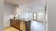 This thoughtfully designed 1-bedroom, 1-bathroom residence offers a cohesive open-concept layout that maximizes every square foot. Light wood-look flooring runs continuously throughout the space, lending warmth and visual continuity. The combined kitchen and living area forms the heart of the home, anchored by a generous peninsula with striking granite countertops that provides both prep space and casual seating. The kitchen is outfitted with stainless steel appliances — including a refrigerator, range, microwave, and dishwasher — complemented by crisp white upper cabinetry and rich wood-toned lower cabinets. Elegant pendant lighting above the peninsula adds a refined touch, while a ceiling fan keeps the living area comfortable. Large windows and a glass-panel exterior door flood the living space with natural light and provide outdoor access. Crown molding throughout elevates the overall finish of the space. The bedroom is a comfortable retreat, featuring a ceiling fan, a bright window with blinds, and crown molding consistent with the rest of the home. The bathroom offers a granite-topped vanity with wood cabinetry, a full bathtub, and clean tile work. An adjacent closet provides practical storage to complete this well-appointed residence.