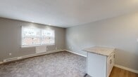 This single-floor studio unit at 161 Anton St in Bridgeport, Connecticut, offers a thoughtfully designed open-concept layout that efficiently combines the living and kitchen areas. The main living space is finished with neutral gray carpeting and light gray walls, creating a calm, cohesive atmosphere throughout. A window along one wall allows natural light to fill the room, offering views of the surrounding neighborhood.

The kitchen is defined by a peninsula with granite countertops, which serves as a natural divider between the cooking and living areas. White cabinetry provides ample storage, while a classic subway tile backsplash adds a clean, modern touch. Stainless steel appliances — including a refrigerator, stove, microwave, and sink with a contemporary faucet — complete the well-appointed kitchen.

The bathroom is accessible via a hallway off the main living area and features wood-look plank flooring, a full bathtub with a shower, and a clean white finish throughout. Baseboard heating is present in both the living area and bathroom, ensuring year-round comfort. The overall design is neutral and move-in ready, providing a practical and comfortable living environment in Bridgeport's residential landscape.