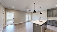 Located at 2121 Langhorne Rd in Lynchburg, Virginia, this thoughtfully designed single-floor unit offers a comfortable and modern living experience. The open-concept layout seamlessly connects the kitchen and living area, creating an inviting and functional space. The kitchen is a standout feature, showcasing gray shaker-style cabinetry with matte black hardware, crisp white quartz countertops, a subway tile backsplash, stainless steel appliances, and a central island with a built-in sink and stylish pendant lighting overhead. Light hardwood-style flooring flows throughout the main living areas, complementing the neutral color palette. The living area benefits from natural light streaming through a set of French doors, and a ceiling fan adds comfort year-round. The bedroom is a well-sized retreat, carpeted for warmth, with large windows, a ceiling fan, and a double-door closet providing generous storage. The full bathroom is clean and contemporary, featuring gray cabinetry with a white countertop vanity, matte black fixtures, light wood-style flooring, and a full tub-shower combination. A dedicated utility room with washer and dryer hookups adds everyday convenience to this efficiently designed home.