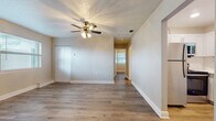 This single-story home presents a clean, updated interior with consistent wood-look laminate flooring running throughout every room, creating a cohesive and low-maintenance living environment. Neutral-toned walls and white baseboards complement the light flooring, contributing to a bright and airy atmosphere across the entire floor plan.

The main living area is spacious and well-lit, featuring a ceiling fan with integrated lighting and a textured ceiling. A louvered bifold closet door provides convenient built-in storage within this central space, while a hallway leads toward the rest of the home.

The kitchen is thoughtfully appointed with white shaker-style cabinetry, a classic subway tile backsplash, light countertops, a stainless steel sink, and a stainless steel range. A window above the sink allows natural light to fill the workspace.

Multiple bedrooms are distributed throughout the home, each featuring windows with blinds that invite natural light. Several bedrooms include ceiling fans and closet storage, with at least one room offering a built-in open closet with shelving.

The bathroom is outfitted with a white vanity, a full tub-shower combination with chrome fixtures, a window for ventilation and natural light, and matching wood-look flooring, maintaining the home's cohesive design aesthetic.