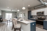 This single-floor residence offers a thoughtfully designed open-concept layout that seamlessly connects the kitchen, dining, and living areas. The kitchen is a standout feature, showcasing two-tone cabinetry with navy lower cabinets and crisp white upper cabinets, complemented by a mosaic tile backsplash, quartz countertops, and a full suite of stainless steel appliances. A spacious island with an undermount sink and seating for two serves as a natural gathering point. Exposed ductwork adds an industrial accent to the otherwise contemporary aesthetic throughout.

The living room is bright and inviting, with light wood-style flooring, a ceiling fan, and sliding glass doors that open to a private balcony offering open exterior views. Both bedrooms are well-proportioned, each with large windows that bring in generous natural light, ceiling fans, and easy access to their respective bathrooms. The bathrooms feature dark navy cabinetry, white quartz vanity tops, light wood-style tile flooring, and well-lit mirrors. The primary bathroom connects directly to a spacious walk-in closet with wire shelving. Neutral tones throughout create a cohesive, modern ambiance.