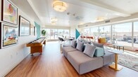 Located at 521 W Colorado St in Glendale, CA, this single-floor community lounge is a thoughtfully designed, multifunctional gathering space that combines modern aesthetics with practical amenities. Rich hardwood flooring runs throughout, providing a warm foundation that contrasts beautifully with the crisp white ceilings and walls.

The space is immediately distinguished by its bold, geometric wall murals rendered in teal, cobalt blue, red, and yellow, adding a dynamic and artistic energy to the interior. Flush drum ceiling fixtures provide consistent, even lighting that complements the generous natural light pouring in through large windows along the front-facing wall, offering open views of the surrounding Glendale streetscape.

The lounge is organized into several distinct zones. A comfortable seating area features a large sectional sofa with coordinating accent pillows, ideal for casual gatherings. A pair of high-back upholstered privacy chairs with side tables offers a quieter nook for focused work or conversation. A shuffleboard table and a wall-mounted TV add recreational and entertainment value. A dining and collaborative work area with tables and chairs supports group activities, while a built-in credenza with a wall-mounted display screen serves as a central information hub. A curated gallery wall of framed artwork further enhances the creative atmosphere of this well-appointed communal space.