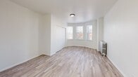 Located at 7715 S South Shore Drive in Chicago's South Shore neighborhood, this one-bedroom, one-bathroom unit offers a thoughtfully organized layout across a single floor. The interior is finished with light wood-style flooring throughout, crisp white walls, and clean white trim, creating a bright and cohesive aesthetic.

The combined living and dining area is the focal point of the unit, featuring a distinctive bay window that floods the space with natural light and offers views of the surrounding neighborhood. A classic cast-iron radiator adds a charming, period-appropriate architectural detail to the room. The open feel of this area makes it versatile for both living and dining arrangements.

The bedroom is a well-proportioned private retreat, equipped with a sliding closet and a window fitted with blinds for light control and privacy. An additional closet elsewhere in the unit provides extra storage. The kitchen, visible from the main living area, features warm-toned cabinetry and provides a functional cooking space.

The bathroom maintains the unit's clean aesthetic with all-white tile surrounding a bathtub/shower combination, a window for natural ventilation, and a vanity with sink. Throughout the unit, the consistent use of light tones and natural light contributes to an airy, welcoming ambiance well-suited to comfortable urban living.