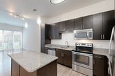 Located at 15955 Frederick Rd in Rockville, MD, this thoughtfully designed one-bedroom residence offers a modern and efficient layout across a single floor. The open-concept kitchen serves as the centerpiece of the home, showcasing rich dark-espresso cabinetry that extends to the ceiling for generous storage, granite countertops, and a full suite of stainless steel appliances including an electric range, built-in microwave, dishwasher, and refrigerator. A substantial kitchen island with a matching granite surface and built-in outlets provides additional prep space and casual seating potential, while elegant pendant lighting overhead adds a refined touch. Light wood-style flooring runs throughout the main living areas, complementing the bright, neutral color palette and contributing to an airy, contemporary feel. The bedroom offers a comfortable, well-proportioned retreat finished with plush carpeting and a large window fitted with blinds that frame outdoor views and allow for an abundance of natural light. A dedicated closet provides practical storage. The clean lines, modern finishes, and efficient use of space throughout create a cohesive and inviting living environment well-suited for comfortable everyday living.