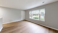 Located at 1909 Cambridge Dr in Lexington, Kentucky, this well-appointed single-story home offers a thoughtfully designed layout comprising a combined kitchen and living area, one bedroom, one bathroom, and a closet. Light wood-look flooring flows consistently throughout the entire home, creating a clean, cohesive aesthetic complemented by soft gray walls and crisp white trim.

The living room is a welcoming, open space anchored by a large multi-pane window that frames views of mature greenery outside, filling the room with abundant natural light. The entry door opens directly into this area, making for a bright and accessible arrival.

The galley-style kitchen is efficiently arranged with white cabinetry featuring matte black hardware, a light stone-topped sink, and a full suite of appliances including a refrigerator and range. Overhead lighting keeps the space well-lit throughout the day.

The bedroom is generously sized with two windows on adjacent walls, allowing for excellent cross-ventilation and natural light from multiple directions. A dedicated closet with louvered doors provides practical storage.

The bathroom is finished in a clean, modern style with white fixtures, a tub-shower combination with a rainfall showerhead, matte black accents, and a white vanity with matching hardware. A window above the tub adds natural light to the space. The overall design is fresh, functional, and move-in ready.
