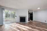 This single-floor residence offers a clean, neutral design with a practical and comfortable layout. The open living area welcomes you with warm wood-look flooring, soft natural light from a sliding glass door that leads to the outdoors, and a front entry door — creating an inviting, airy atmosphere. The galley-style kitchen is thoughtfully designed with rich dark cabinetry lining both sides, white countertops, a stainless steel sink, and black appliances including a range and refrigerator. A window above the dining area allows natural light to fill the space. The bedrooms are generously sized, finished with plush carpeting underfoot, and each features a walk-in closet for ample storage. Baseboard heating units and windows with blinds are present in the bedrooms, offering both comfort and privacy. The bathroom is neatly appointed with a dark wood vanity, white countertop, a large mirror with overhead lighting, and a full tub-shower combination. Neutral tones are carried throughout the home, lending a cohesive and calming ambiance. The space also includes a dedicated hallway connecting the main living areas to the private quarters, contributing to a sensible and functional flow throughout.