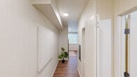 This well-designed single-floor unit offers a cohesive modern aesthetic characterized by clean lines, a neutral warm palette, and wood-look flooring that flows seamlessly throughout the space. The entry hallway sets an inviting tone, featuring recessed circular lighting, crisp white walls, and tasteful wall art that leads naturally into the main living areas. The kitchen is efficiently laid out and outfitted with light natural wood cabinetry, white countertops, and a full suite of stainless steel appliances including a refrigerator, electric range, over-the-range microwave, and dishwasher. A window above the counter brings in natural light, enhancing the kitchen's bright and functional feel. The bedroom is a comfortable, well-lit retreat with a large window that allows abundant natural light to fill the room. It comfortably accommodates a bed and a workspace, making it versatile for both rest and productivity. The bathroom is clean and modern, featuring a floating wood-toned vanity with an integrated white sink, a large wall mirror with overhead lighting, grab bars, and a shower-tub combination. Recessed lighting throughout the unit ensures consistent, even illumination, while the open layout between the kitchen and living area promotes an airy, connected sense of space.