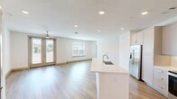 Located in Huntersville, NC, this well-appointed 2-bedroom, 2-bathroom single-story home offers a thoughtfully designed open-concept layout with generous living space throughout. The heart of the home is a bright kitchen and living area, where light wood-tone flooring, recessed lighting, and crisp white walls create a clean, modern aesthetic. The kitchen features a large center island with an integrated sink and light quartz countertop, taupe shaker-style cabinetry, stainless steel appliances including a French door refrigerator and built-in microwave, and a seamless flow into the expansive living room. The living room is enhanced by a ceiling fan, built-in floating shelves, and a built-in desk nook, adding both function and character. Each bedroom is carpeted for comfort and includes a ceiling fan and natural light from well-positioned windows. The primary bedroom connects to a private en-suite bathroom outfitted with wood-tone flooring, a single vanity with white countertop, brushed nickel fixtures, and a glass-enclosed shower, which leads directly into a spacious walk-in closet with custom shelving and multiple hanging rods. The second bathroom mirrors the same refined finishes, also providing direct access to a well-organized walk-in closet. The exterior features a wide driveway with lush green landscaping.