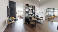 This thoughtfully designed single-floor community amenity space offers a rich variety of gathering areas, each with its own distinct character and purpose. Wide-format wood-look tile flooring runs throughout, creating a cohesive and polished foundation across all areas.

The central lounge is anchored by a dramatic floor-to-ceiling stacked stone fireplace with a wood mantel, complemented by soaring ceilings, a statement chandelier, and warm leather seating. Adjacent to it, a cozy reading nook features a built-in bookcase, velvet sofa, and pendant lighting, offering a more intimate setting.

The kitchen area is outfitted with dark cabinetry, white quartz countertops, a subway tile backsplash, open floating shelves, a center island, and stainless steel appliances — ideal for entertaining or casual use.

A dedicated business center includes computer workstations, built-in display shelving, high-top seating, and a glass-top conference table beneath a stylish brass chandelier, making it a functional workspace. A connected media room with a wall-mounted TV, whitewashed brick accent wall, and large windows with a built-in window seat adds another versatile gathering option.

The billiards room rounds out the space with a full-size pool table, wall-mounted cue rack, curated artwork, and a rectangular industrial chandelier above.