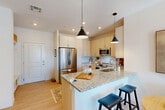 This thoughtfully designed 2-bedroom, 2-bathroom residence in Waltham, MA offers a bright and modern living experience across a single floor. The open-concept layout seamlessly connects the kitchen, dining area, and living room, all finished with light hardwood-style flooring that enhances the airy ambiance. The kitchen is a standout, featuring granite countertops, light wood cabinetry extending to the ceiling, stainless steel appliances including a range, microwave, and refrigerator, and a peninsula with bar seating illuminated by stylish pendant lighting. The living area is filled with natural light from large windows overlooking the surrounding community. The primary bedroom offers plush carpeting, warm accent walls, and direct access to a well-organized walk-in closet with built-in shelving and drawers. The en-suite bathroom includes granite countertops, light wood cabinetry, and a shower-tub combination. The second bedroom is equally bright, with generous window views. A second full bathroom mirrors the same refined finishes. Additional conveniences include dedicated closets, a utility room, and in-unit laundry, rounding out this well-equipped and comfortable Waltham residence.