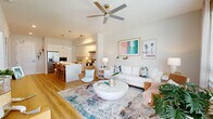 Located in Saint Petersburg, FL, this well-appointed one-bedroom, two-bathroom residence offers a thoughtfully designed open-concept layout filled with natural light and modern coastal charm. The combined kitchen and living area forms the heart of the home, showcasing warm wood-look flooring, a ceiling fan, and large windows dressed with sheer curtains that bathe the space in sunlight. The living room provides a welcoming atmosphere with ample room for comfortable seating and stylish decor. The kitchen is a standout feature, boasting sleek white cabinetry extending to the ceiling, stainless steel appliances including a refrigerator, dishwasher, and range, along with a generous island with built-in shelving and bar seating — ideal for casual dining or entertaining. The spacious bedroom is a serene retreat finished with plush carpet, a ceiling fan, and floor-to-ceiling sliding glass doors that open directly onto a private balcony with outdoor views. A dedicated closet provides practical storage. Both bathrooms are finished in crisp white tones with modern floating vanities and clean tile flooring. A dedicated laundry area adds everyday convenience. Hallways connect the spaces efficiently, and the private balcony offers a pleasant outdoor extension of the living space.