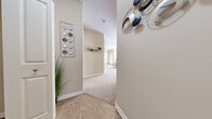 This single-floor residence offers a thoughtfully designed layout encompassing two bedrooms, two bathrooms, a combined living and dining area, and a kitchen. The entry hallway features tile flooring and neutral warm-beige walls, transitioning to plush carpet throughout the main living spaces. The kitchen is equipped with warm wood cabinetry, black appliances including a refrigerator, range, and over-the-range microwave, and a breakfast bar with seating — ideal for casual dining. Adjacent to the kitchen, the dining area provides a cozy nook, while the living room offers a comfortable gathering space with a ceiling fan, a bright window allowing natural light, and soft carpet underfoot. The primary bedroom is a generously proportioned retreat featuring carpet flooring, a ceiling fan, and access to a closet with built-in shelving. The second bedroom mirrors the comfortable aesthetic of the primary. Both bathrooms feature tile flooring and a clean, functional design, with at least one bathroom offering a glass-enclosed shower. Throughout, the consistent warm neutral palette and white trim create a cohesive and welcoming ambiance suitable for a variety of living arrangements.