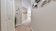 This single-floor residence offers a thoughtfully designed layout encompassing two bedrooms, two bathrooms, a combined living and dining area, and a kitchen. The entry hallway features tile flooring and neutral warm-beige walls, transitioning to plush carpet throughout the main living spaces. The kitchen is equipped with warm wood cabinetry, black appliances including a refrigerator, range, and over-the-range microwave, and a breakfast bar with seating — ideal for casual dining. Adjacent to the kitchen, the dining area provides a cozy nook, while the living room offers a comfortable gathering space with a ceiling fan, a bright window allowing natural light, and soft carpet underfoot. The primary bedroom is a generously proportioned retreat featuring carpet flooring, a ceiling fan, and access to a closet with built-in shelving. The second bedroom mirrors the comfortable aesthetic of the primary. Both bathrooms feature tile flooring and a clean, functional design, with at least one bathroom offering a glass-enclosed shower. Throughout, the consistent warm neutral palette and white trim create a cohesive and welcoming ambiance suitable for a variety of living arrangements.