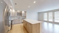 Located at 7680–7698 S New Braunfels Ave in San Antonio, TX, this thoughtfully designed one-bedroom, one-bathroom unit offers a clean, modern aesthetic throughout. Light wood-tone flooring flows seamlessly across the entire floor plan, complementing the bright white walls and recessed lighting that keep the space feeling open and airy.

The open-concept kitchen is a standout feature, showcasing light wood cabinetry with sleek hardware, a tiled backsplash, white quartz countertops, stainless steel appliances including a range, microwave, and dishwasher, and a generous center island ideal for dining or meal prep. The kitchen connects naturally to the living area, which benefits from large windows that invite abundant natural light.

The spacious primary bedroom includes a ceiling fan, large windows with blinds, and direct access to an expansive private balcony. The balcony, finished with wood-tile decking and a metal railing, offers sweeping open views of the surrounding San Antonio landscape — a rare outdoor retreat. The walk-in closet provides well-organized built-in shelving and hanging rods for ample storage.

The bathroom is finished with a wood-framed mirror, light wood vanity with quartz countertop, a combined tub and shower, and consistent light wood flooring. The overall ambiance is clean, contemporary, and move-in ready.