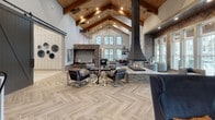 Located at 145 Legends Club Lane in Franklin, Tennessee, this single-story clubhouse showcases a refined modern farmhouse aesthetic throughout its expansive layout. The entry foyer welcomes visitors through glass-paned double doors flanked by floor-to-ceiling windows dressed in sheer drapery, with herringbone-patterned tile flooring establishing an elegant tone from the start. Dramatic sliding barn doors in a dark charcoal finish open to a broad corridor lined with statement chandeliers and recessed lighting.

The main gathering hall commands attention with soaring vaulted ceilings supported by exposed wooden beams, a striking suspended fireplace as a central focal point, and herringbone tile flooring. White shiplap walls, stacked stone accents, and rustic wood columns contribute layers of texture throughout. An adjacent lounge area features soaring two-story windows, a wall-mounted TV set into a wood-paneled surround, leather seating, and abundant natural light with outdoor views.

Additional seating nooks offer intimate settings with large windows overlooking the surrounding community. A well-appointed kitchen area includes stainless steel appliances, stone countertops, pendant lighting, and wood-paneled cabinetry. A separate dining and event room provides flexible space with mixed seating, a presentation screen, and direct exterior access, completing this thoughtfully designed communal facility.