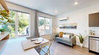 This thoughtfully designed studio unit combines a kitchen, dining, and living area into one efficient, open-plan layout. Light wood-tone flooring runs throughout, complementing the crisp white walls and recessed lighting to create a bright, airy atmosphere. Large windows along the living area wall frame lush tree canopy views, flooding the space with abundant natural light and providing a refreshing connection to the outdoors. Linen drapes add a soft, modern touch.

The kitchen is outfitted with dark wood cabinetry, granite-look countertops, a white subway tile backsplash, and a full suite of stainless steel appliances, including a range, microwave, and refrigerator. A compact dining area sits beside the windows, accompanied by built-in wall shelving ideal for storage or display.

The living zone accommodates a sofa and is equipped with a wall-mounted mini-split HVAC unit for year-round climate control. A dedicated closet provides practical storage.

The bathroom features wood-look tile flooring, a dark-tiled tub and shower surround with striking contrast against the white fixtures, a granite-topped vanity with matching dark cabinetry, and tasteful modern wall art. Every element of this studio reflects a clean, contemporary aesthetic with efficient use of space.