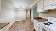 This single-floor residence offers a practical and well-organized layout across three bedrooms and two bathrooms. Wood-style plank flooring runs throughout the main living and kitchen areas, providing a warm, cohesive aesthetic, while plush carpet covers all three bedrooms.

The kitchen features white cabinetry with ample upper and lower storage, dark granite-style countertops, a stainless sink, and white appliances including a range and refrigerator. It opens directly to the dining area, which is accented by a chandelier pendant light and a two-tone wall treatment with a chair rail detail.

The generously sized primary bedroom includes a sliding glass door that opens to an outdoor view of mature trees, offering a pleasant natural backdrop. The two additional bedrooms each feature ceiling fans with light fixtures, vertical blind-covered windows allowing natural light, and neutral carpeting.

Both bathrooms continue the wood-style flooring. One bathroom includes a tiled shower-tub combination with chrome fixtures, while the second is a more compact space. Two closets and two hallways provide functional storage and traffic flow throughout the home, contributing to an efficient and livable floor plan.
