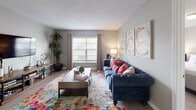 This apartment showcases a harmonious blend of modern design and comfort. The living room boasts a plush blue sofa, colorful abstract art, and a vibrant area rug, creating a lively ambiance. The kitchen features white cabinetry, black appliances, and a stylish herringbone backsplash. The bedroom offers a serene retreat with a comfortable bed, contemporary artwork, and ample natural light. The bathroom continues the modern theme with a blue and white striped shower curtain and clean lines. Throughout the space, large windows allow for plenty of natural light, enhancing the open and airy feel of the apartment.