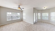 This single-floor residence offers a thoughtfully designed layout that balances comfort and functionality throughout. The spacious living area is finished with plush wall-to-wall carpeting and neutral gray walls, bathed in natural light from multiple windows fitted with white blinds. A ceiling fan with an integrated light fixture provides both airflow and ambient lighting, while a sliding glass door provides access to the outdoors.

The kitchen is a functional highlight, featuring rich medium-toned wood cabinetry paired with dark granite countertops and a breakfast bar with pendant lighting overhead. Black appliances, including a refrigerator, range, and dishwasher, complement the wood-look flooring that flows through this space. A pass-through opening connects the kitchen to the living area, enhancing the open feel of the home.

The bedrooms are carpeted and generously sized, with clean lines and neutral finishes. At least one bedroom includes a walk-in closet with built-in shelving and hanging rods, offering ample storage. The bathroom features warm tile flooring, a wide vanity with rich wood cabinetry, a light stone countertop, a large mirror, and stylish overhead lighting. Overall, the space presents a clean, move-in ready environment with a cohesive and practical design throughout.