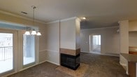 This two-story home in Lewisville, Texas is designed with a functional and connected layout across both levels. The main living area is a highlight of the home, showcasing a striking double-sided fireplace clad in warm tile, which serves as a central architectural feature dividing the dining and living spaces. The fireplace's structural column extends to the ceiling, adding visual height and a sense of definition between the two areas without fully closing them off.

Crown molding runs throughout the main level, adding a refined detail to the neutral-toned walls. Carpet flooring extends across the living and dining areas, while tile flooring is laid beneath and around the fireplace. A decorative pendant chandelier illuminates the dining area, which receives natural light through a window fitted with blinds.

An arched passageway connects the main living space to an additional room, which benefits from natural light through a glass-paneled front door. Ceiling fans are present in the living areas, supporting air circulation throughout. The overall ambiance of the main level is warm and cohesive, with traditional design elements that complement the open, flowing arrangement of the space.