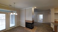 This two-story home in Lewisville, Texas is designed with a functional and connected layout across both levels. The main living area is a highlight of the home, showcasing a striking double-sided fireplace clad in warm tile, which serves as a central architectural feature dividing the dining and living spaces. The fireplace's structural column extends to the ceiling, adding visual height and a sense of definition between the two areas without fully closing them off.

Crown molding runs throughout the main level, adding a refined detail to the neutral-toned walls. Carpet flooring extends across the living and dining areas, while tile flooring is laid beneath and around the fireplace. A decorative pendant chandelier illuminates the dining area, which receives natural light through a window fitted with blinds.

An arched passageway connects the main living space to an additional room, which benefits from natural light through a glass-paneled front door. Ceiling fans are present in the living areas, supporting air circulation throughout. The overall ambiance of the main level is warm and cohesive, with traditional design elements that complement the open, flowing arrangement of the space.